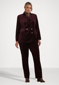 Bordo aksomo dvitakčio kostiumo su blizgiais mygtukais, pritaikytu tinkamu dydžiu ir šoninėmis kišenėmis; derinamas su raštuota šaliku ir rudiems aukštakulniais.