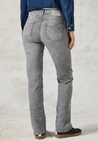 Grijze jeans met een vervaagde textuur, slim fit, met achterzakken en een label op de tailleband. Gepaard met donkere sneakers.