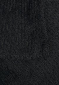 Tissu noir texturé avec une finition douce et duveteuse. Présente un motif nervuré et des bords lisses. Convient à diverses applications textiles.