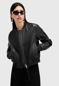 Chaqueta bomber de cuero negro con cremallera frontal, puños y dobladillo acanalados; cuenta con bolsillos laterales y una textura suave.