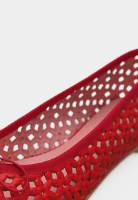 Κόκκινο πλεκτό μπαλαρίνα με λεπτομέρεια φιόγκου και επάνω μέρος με διαπνέον, πλεγμένο μοτίβο πάνω σε ανοιχτό φόντο.