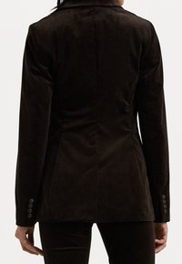 Brązowa marynarka z sztruksu o dopasowanym kroju, z klapą z wcięciem, mankietami na guziki i widocznymi detalami szwów na plecach.