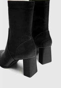 Bottines noires à talons en cuir lisse avec un talon carré à bloc, présentant un design épuré et des détails de couture subtils.