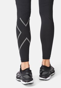 Sorte atletiske leggings med grå diagonale mønstre, parret med sorte løbesko med teksturerede detaljer og hvid polstring.