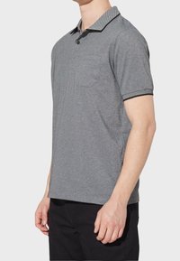 Polo gris à manches courtes avec poche, doté d'un tissu texturé, d'un col contrasté et d'accents noirs sur les manches.