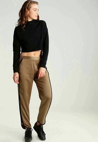 Must musta, millel on külgedel mustad triibud, ja beežid jogger püksid. Jogger püksid on lõdva lõikega ja valmistatud siledast kangast. Mustad tennisekingad.