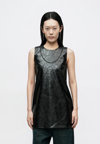 Svart ermeløs tunika i blankt lær, med rund hals og teksturert svart kjededetalj langs halsen.