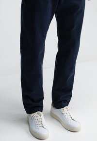 Marineblauwe katoenen broek met een relaxed fit. Gecombineerd met witte leren sneakers met beige accenten en een gestructureerde zool.
