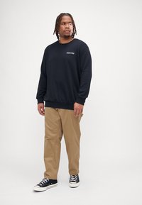 Czarna bluza z wyszywanym logo "Club1990", w połączeniu z khaki spodniami i czarnymi trampkami z białą podeszwą. Prosty design i luźny krój.