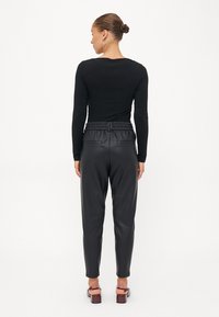 Zwarte lange mouw top met een getailleerd ontwerp, gecombineerd met zwarte faux lederen tapered pants met een elastische tailleband en twee achterzakken.