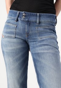 Jeans in denim azzurro chiaro con un design aderente, dotati di zip e due tasche frontali. Leggermente sbiaditi con dettagli di cuciture a contrasto.