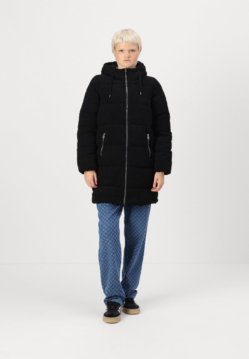 Manteau matelassé noir avec une capuche, poches zippées et une fermeture éclair à l'avant. Assorti avec un pantalon bleu à motifs et des baskets noires à semelle en gomme.
