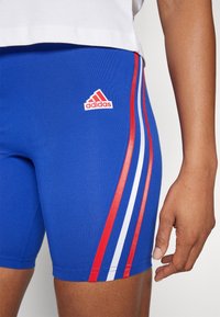 Adidas blå sportshorts med röda och vita sidostrikar och en liten röd logotyp på vänster lår. Tillverkade av elastiskt material.