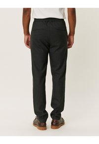 Pantalons ajustés gris foncé avec une taille élastique, deux poches arrière et une coupe droite, présentant une texture lisse.