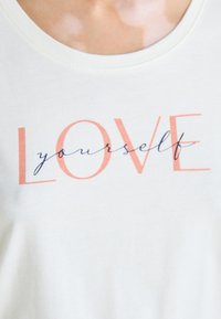 Camisola branca de algodão sem mangas com o texto "AMOR" em laranja e "a ti mesmo" em azul marinho em caligrafia, com decote redondo.