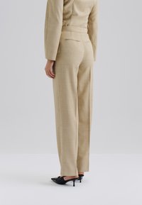 Pantalons beige ajustés en tissu texturé, présentant une coupe droite et des poches arrière. Associés à des escarpins noirs à bout pointu.