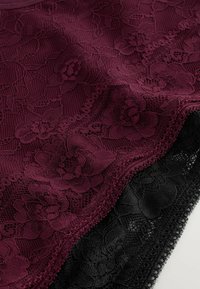 Tissu en dentelle florale bourgogne et noir avec des bords festonnés, superposé de motifs floraux complexes et de détails en maille fine.
