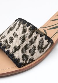 Gros plan sur une sandale de type mule beige avec une sangle en tissu à imprimé animal noir et beige et une petite étiquette métallique "PEPE JEANS" attachée.