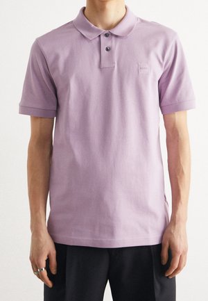 Lilafarbenes Polohemd mit klassischem Kragen, Knopfleiste mit zwei Knöpfen und kurzen Ärmeln. Verfügt über ein dezentes Logo auf der Brust und besteht aus weichem Baumwollmaterial.