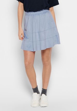 Vrouw met een lichtblauwe minirok met elastische taille, donkergrijze sokken, witte sneakers en een zwart topje, vanaf de taille naar beneden afgebeeld.
