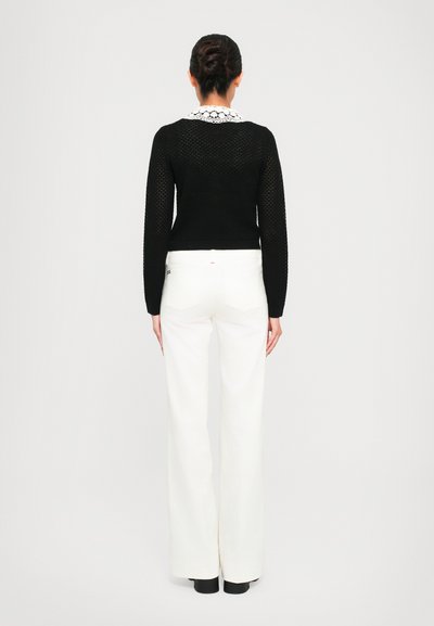 Black knitted sweater with long sleeves and a white lace collar, paired with high-waisted white wide-leg pants and black shoes.