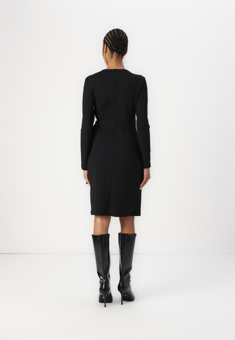 Vestido negro de manga larga con silueta ajustada, hasta la rodilla y diseño de espalda sin costuras, combinado con botas brillantes hasta la rodilla.