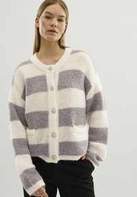 Cardigan lavorato a maglia con strisce bianche e grigie morbide, caratterizzato da un colletto a V, cinque bottoni e due tasche frontali. Tessuto testurizzato con un aspetto accogliente.