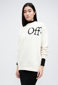 Κρεμ πουλόβερ πλεκτό με χαλαρή εφαρμογή, που παρουσιάζει ένα μεγάλο μαύρο λογότυπο "Off." στο μπροστινό μέρος. Οι ραβδωτές μανσέτες και το τελείωμα προσθέτουν υφή.