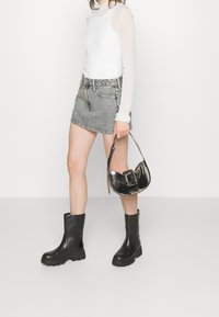 Black knee-high rubber boots, light grey denim shorts, and a fitted white long-sleeve top. Holding a small black patent handbag.