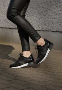 Černé sportovní tenisky vyrobené z texturované tkaniny a hladké kůže, s bílou podrážkou, tkaničkami a jemnými designovými akcenty.