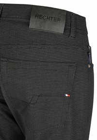 Pantalons noirs texturés avec une étiquette en cuir, des poches arrière et de subtils détails de couture blanche.