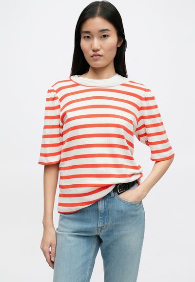 Κόκκινο και λευκό ριγέ μπλουζάκι με κοντά μανίκια, ριγέ υφή, στρογγυλή λαιμόκοψη και άνετη γραμμή, συνδυασμένο με ανοιχτό μπλε τζιν.