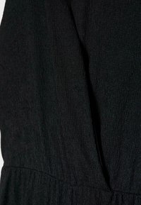Gros plan d'un tissu noir texturé avec une couture et un léger froncé près du bord inférieur.