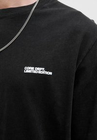 Sort bomulds T-shirt med rund halsudskæring og korte ærmer. Hvid tekst på forsiden siger "CORE DEPT. LIMITED EDITION".