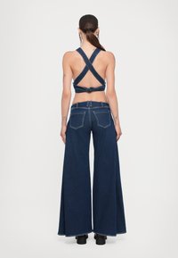 Denim kratka majica s križnim trakama i čvorastim detaljem, u kombinaciji s tamnim širokim trapericama. Ima pet džepova i kontrastnu šavovu.