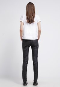 Vit kortärmad topp i kombination med svarta smala läderbyxor. Toppen har en rak skärning, och byxorna har detaljer med bakfickor.