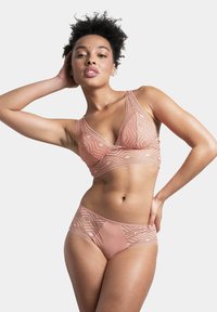Ensemble de bralette en dentelle et de bikini assorti en rose blush. Des motifs géométriques ornent le tissu, mettant en avant des textures douces et un design soutenant.