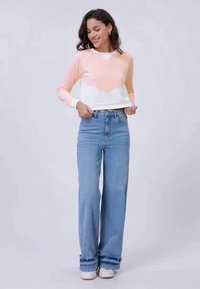 Maglione leggero in arancione pastello e bianco con un design a forma di V. Abbinato a jeans azzurri a vita alta e gamba dritta e sneakers bianche.