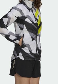 Lett jakke med sort, hvid og gråt geometrisk mønster og neongule accenter. Har lynlåslukning og sidelommer.