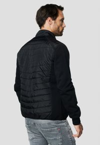 Čierna bunda s prešívaným zadným dielom a moderným dizajnom. Rukávy sú z hladkej tkaniny, čo dopĺňa celkový monochromatický vzhľad.