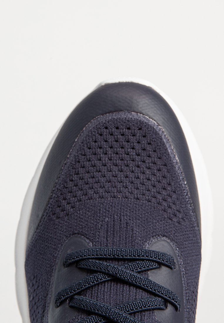Chaussure de sport bleu marine foncé avec un dessus en maille respirante, des accents en cuir lisse et des lacets texturés, dotée d'une semelle blanche.