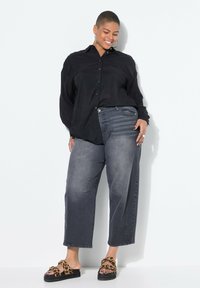 Czarna koszula z guzikami o luźnym kroju, zestawiona z postarzanymi, szarymi spodniami typu wide-leg. Obuwie w panterkę z masywną czarną podeszwą.