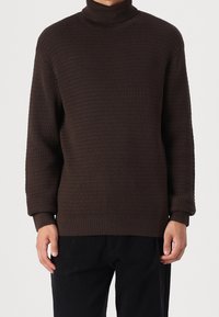 Pull col roulé marron texturé avec poignets et ourlet côtelés, présentant une coupe ample et un motif en maille gaufrée.
