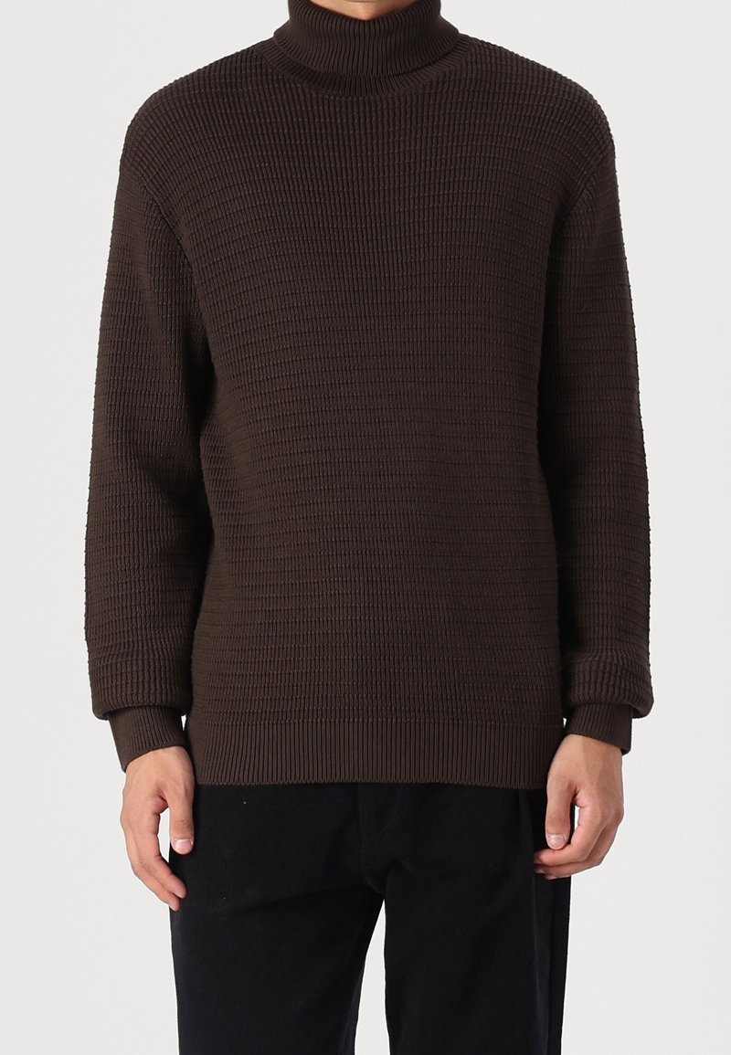 Pull col roulé marron texturé avec poignets et ourlet côtelés, présentant une coupe ample et un motif en maille gaufrée.