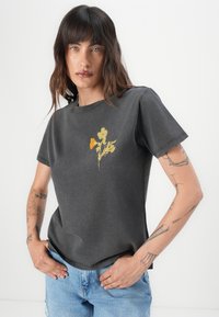 T-shirt in cotone grigio con maniche corte, caratterizzato da una stampa floreale gialla e arancione al centro e una vestibilità comoda.