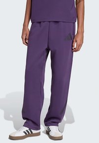 Μωβ παντελόνι τζόγκινγκ από ύφασμα με λεία υφή, με λεπτομέρειες πλευρικών ρίγων και μαύρο λογότυπο στο αριστερό μηρό.