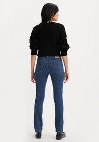 Maglione nero a trecce con maniche a sbuffo, abbinato a un paio di jeans in denim blu con design a cinque tasche e toppa in pelle sul retro.