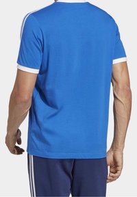 Blå t-shirt med vit krage och ärmkanter. Korta ärmar och en avslappnad passform. Baksidan är slät utan ytterligare mönster eller detaljer.