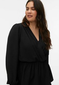 Robe portefeuille noire avec manches longues bouffantes et taille cintrée. Tissu texturé avec une légère brillance, encolure en V et détails drapés.