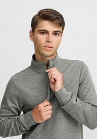 Grå zip-up pullover i mjukt tyg. Har hög krage, långa ärmar och en slimmad passform. Slät yta med minimala sömdetaljer.